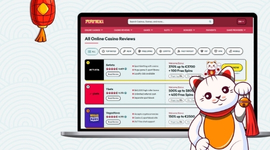 A white maneki-neko cat with a bell in its paw next to a laptop displaying casino reviews.
